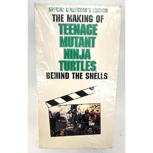 Op de afbeelding: Een rechthoekige VHS-cassettehoes met de titel Special Collector's Edition The Making of Teenage Mutant Ninja Turtles Behind the Shells in groene en zwarte tekst. Een filmklapper-afbeelding bevindt zich boven een foto van de personages.