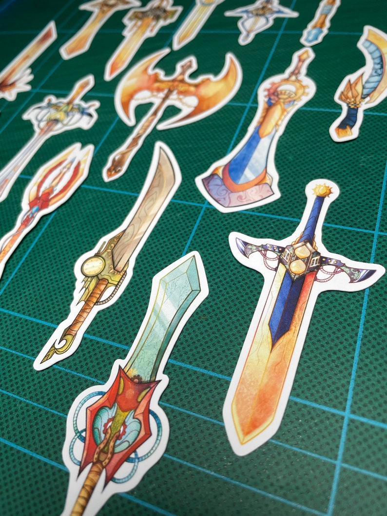 May include: A collection of colorful fantasy sword stickers with intricate details. The stickers feature various designs, including a golden axe, a blue and gold sword with a sun design, and a green and red sword with a crystal tip.