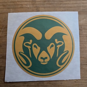 May include: A round sticker featuring a ram's head silhouette in green and gold.
