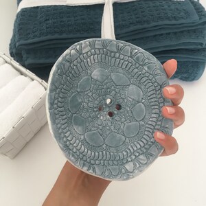 Peut inclure: Un porte-savon en céramique bleu avec un motif de dentelle décoratif et trois trous au centre.