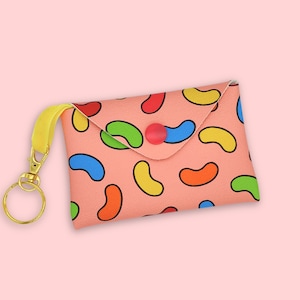May include: A pink fabric keychain with a yellow strap and a gold key ring. The fabric has a pattern of colorful jelly beans.