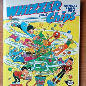 Puede incluir: Un cómic anual de Whizzer and Chips de 1990. La portada presenta un árbol de Navidad con personajes decorándolo. El libro es amarillo con texto azul y rojo.