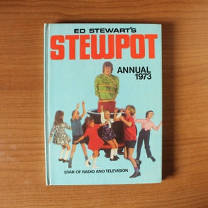 Pode incluir: Uma capa de livro azul e laranja com o título "Ed Stewart's Stewpot Annual 1973" e uma imagem de um homem amarrado em uma panela com crianças ao seu redor. O texto "Star of Radio and Television" está na parte inferior da capa.