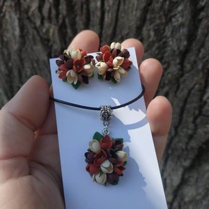 May include: A set of handmade jewelry featuring a necklace and earrings. The necklace has a pendant with a cluster of brown, white, and orange flowers. The earrings are also clusters of brown, white, and orange flowers.