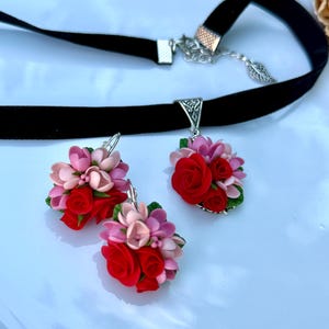 Peut inclure: Un collier ras-du-cou en velours noir et une paire de boucles d'oreilles assorties, orn&eacute;s de grappes de roses rouges et de fleurs rose clair sculpt&eacute;es avec de petites feuilles vertes. Le collier poss&egrave;de un fermoir argent&eacute; et une breloque feuille.