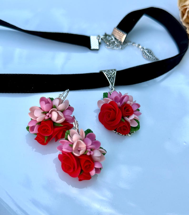Peut inclure: Un collier ras-du-cou en velours noir et une paire de boucles d'oreilles assorties, orn&eacute;s de grappes de roses rouges et de fleurs rose clair sculpt&eacute;es avec de petites feuilles vertes. Le collier poss&egrave;de un fermoir argent&eacute; et une breloque feuille.
