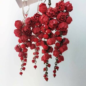 May include: Three pairs of red dangle earrings with flower-shaped charms and red beads hanging from silver and bronze chains.