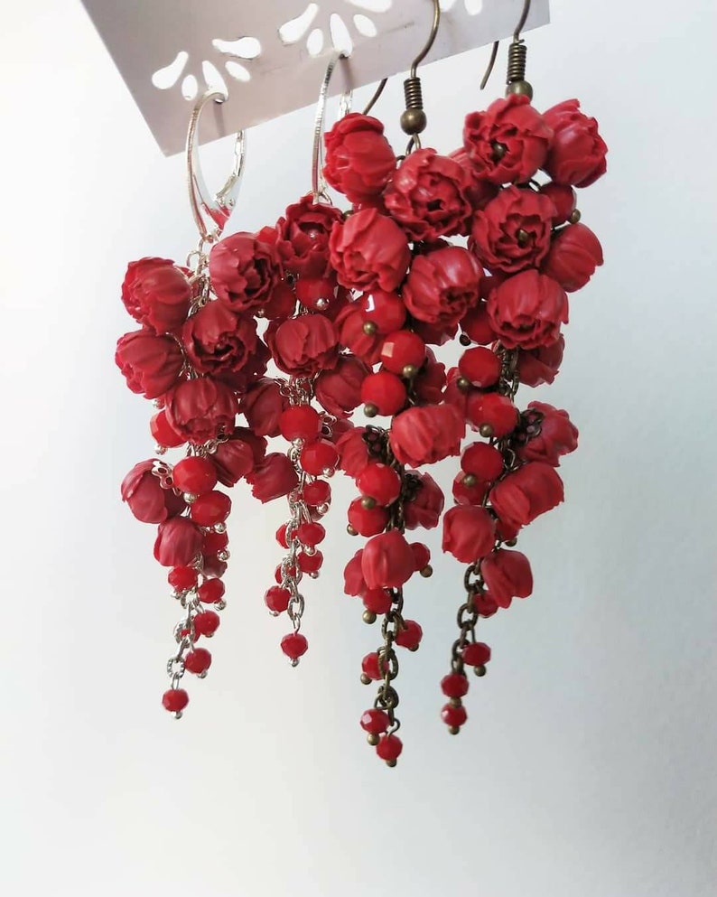 May include: Three pairs of red dangle earrings with flower-shaped charms and red beads hanging from silver and bronze chains.