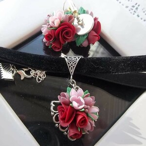 Peut inclure: Un collier ras-du-cou en velours noir et des boucles d'oreilles assorties orn&eacute;es de grappes de roses sculpt&eacute;es rouges et roses avec des feuilles vertes. Les montures en m&eacute;tal argent&eacute; pr&eacute;sentent des d&eacute;tails en filigrane et des fermoirs.