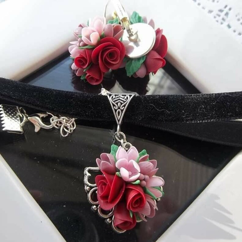 Peut inclure: Un collier ras-du-cou en velours noir et des boucles d'oreilles assorties orn&eacute;es de grappes de roses sculpt&eacute;es rouges et roses avec des feuilles vertes. Les montures en m&eacute;tal argent&eacute; pr&eacute;sentent des d&eacute;tails en filigrane et des fermoirs.
