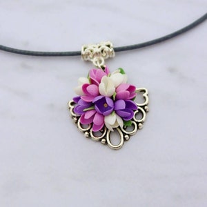 May include: A silver necklace with a floral pendant featuring a cluster of purple, pink, and white flowers. The flowers are arranged in a heart-shaped design and are accented with green leaves.