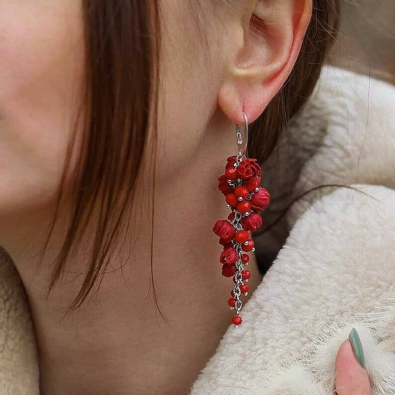 May include: Red beaded earrings with a silver chain and small red flower-shaped beads. The earrings are long and dangle.