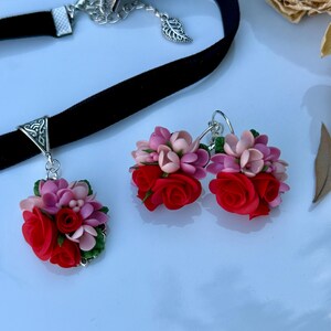 Peut inclure: Un collier ras-du-cou en velours noir avec une b&eacute;li&egrave;re triangulaire argent&eacute;e et un pendentif compos&eacute; de roses rouges et de fleurs roses sculpt&eacute;es avec des feuilles vertes, accompagn&eacute; d'une paire de boucles d'oreilles assorties.