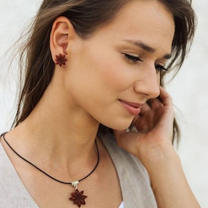 Pode incluir: Uma mulher usando um colar e brincos com um design de anis estrelado. O colar &eacute; feito de cord&atilde;o preto e o pingente &eacute; um anis estrelado. Os brincos tamb&eacute;m t&ecirc;m a forma de anis estrelado.