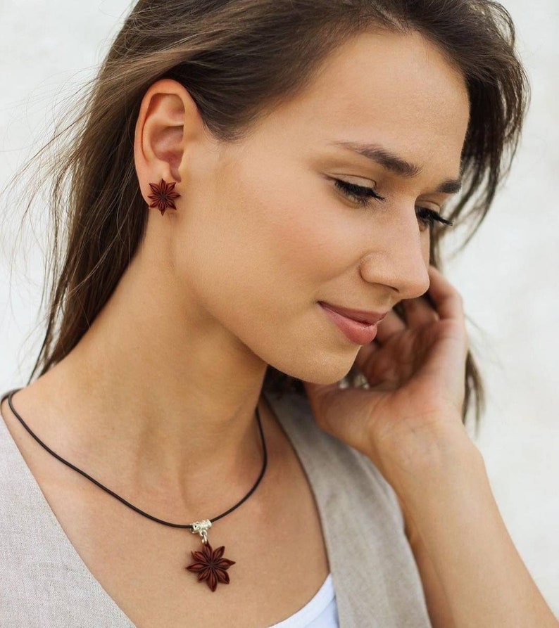 Pode incluir: Uma mulher usando um colar e brincos com um design de anis estrelado. O colar &eacute; feito de cord&atilde;o preto e o pingente &eacute; um anis estrelado. Os brincos tamb&eacute;m t&ecirc;m a forma de anis estrelado.