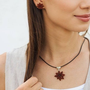 Pode incluir: Um colar com um pingente de anis estrelado marrom em um cord&atilde;o preto e brincos combinando de anis estrelado. O colar tem um fecho prateado.