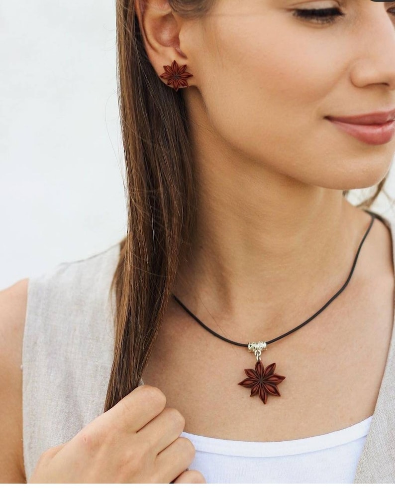 Pode incluir: Um colar com um pingente de anis estrelado marrom em um cord&atilde;o preto e brincos combinando de anis estrelado. O colar tem um fecho prateado.