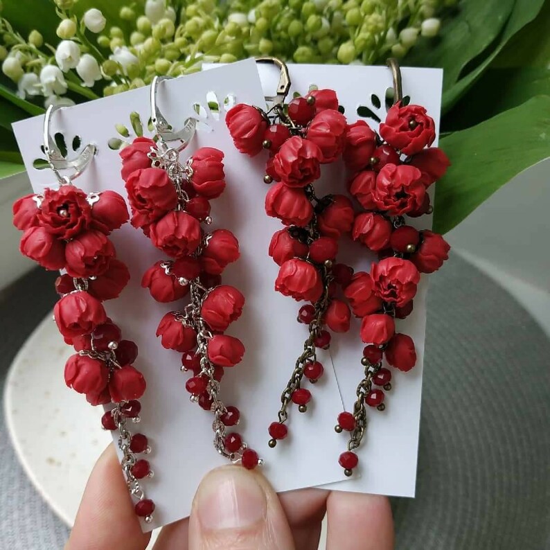 May include: Three pairs of red flower dangle earrings with silver and bronze chains and red crystal beads. The earrings are displayed on white cards.