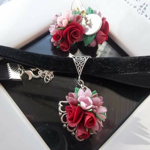 Peut inclure: Un collier ras-du-cou en velours noir et des boucles d'oreilles assorties orn&eacute;es de grappes de roses sculpt&eacute;es rouges et roses avec des feuilles vertes. Le collier poss&egrave;de un pendentif en filigrane argent&eacute; et les boucles ont des fermoirs argent&eacute;s.