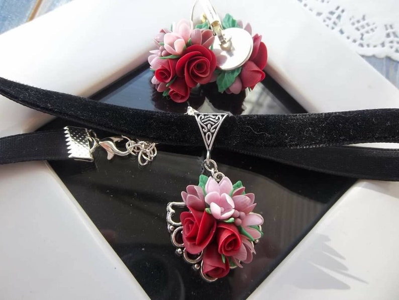 Peut inclure: Un collier ras-du-cou en velours noir et des boucles d'oreilles assorties orn&eacute;es de grappes de roses sculpt&eacute;es rouges et roses avec des feuilles vertes. Le collier poss&egrave;de un pendentif en filigrane argent&eacute; et les boucles ont des fermoirs argent&eacute;s.