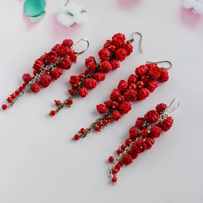 May include: Four pairs of red dangle earrings with a floral design. Each earring features a cluster of small red flowers with a silver chain and red beads.