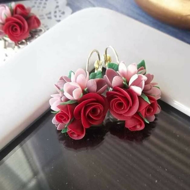 Peut inclure: Une paire de boucles d'oreilles florales compos&eacute;es de grappes de roses rouges sculpt&eacute;es et de fleurs rose p&acirc;le avec de petites feuilles vertes. Les boucles d'oreilles sont fix&eacute;es &agrave; des crochets en m&eacute;tal argent&eacute;. Chaque boucle forme un bouquet.