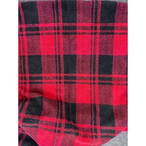 Op de afbeelding: Close-up van een rood en zwart geruite fleece stof. Het patroon heeft grote, gelijkmatig verdeelde vierkanten en rechthoeken in een klassieke lumberjack-stijl. De stof ziet er zacht en warm uit, geschikt voor kleding of woondecoratie.