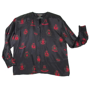 May include: A black long-sleeved button-down shirt featuring a repeating pattern of red circular crests and emblems. The shirt has a round neckline, a front button placket, and buttoned cuffs. The brand label ESCADA is visible at the inner neckline.