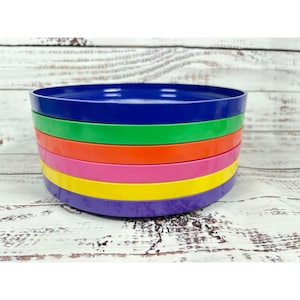 May include: A stack of colorful plastic plates in a rainbow of colors: blue, green, orange, pink, yellow, and purple. The plates are stacked on top of each other, creating a vibrant and eye-catching display. The plates are made of a durable plastic material.