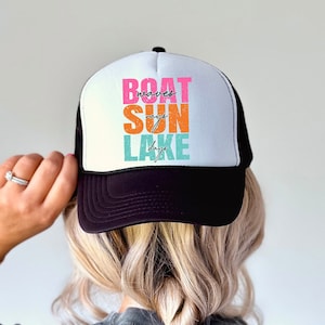 Puede incluir: Gorra de camionero negra con malla blanca en la parte posterior. La parte delantera de la gorra tiene el texto "BOAT waves SUN rays LAKE days" en letras de bloque de colores.