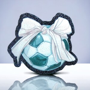 Peut inclure: Un ballon de football bleu et blanc avec un nœud blanc sur le dessus. Le ballon est entouré d'une bordure noire scintillante.