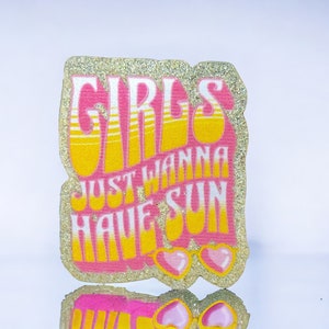 Pode incluir: Um remendo de glitter rosa e amarelo com o texto "Girls Just Wanna Have Sun" e um par de óculos de sol rosa.
