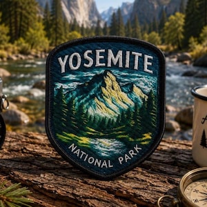 May include: A patch with the text "YOSEMITE NATIONAL PARK" and a mountain landscape design. The patch is blue, green, and yellow, with a black border. Other items in the image include a camera, a mug, and a compass, all on a wooden surface.