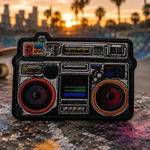 Puede incluir: Parche bordado con un diseño de radiocasete retro. El parche negro tiene detalles coloridos, incluyendo detalles rojos, naranjas, azules y verdes. Los altavoces tienen centros rojos y morados. El parche es para ropa o accesorios.