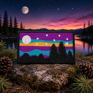 May include: A rectangular embroidered patch featuring a night landscape with a white moon and white stars against a purple sky. Below the sky are horizontal bands of teal and yellow, with black silhouettes of pine trees and mountains at the base.