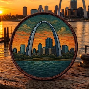 May include: Embroidered patch featuring the Gateway Arch and the St. Louis skyline at sunset. The patch is round with a brown border, showcasing a detailed cityscape in shades of blue, orange, and green. The arch is white and gray.