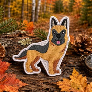 May include: An embroidered patch shaped like a German Shepherd dog. The dog has tan and black fur, pointed ears, a black muzzle, and a small pink tongue visible. The patch features a white stitched border outlining the entire canine figure.