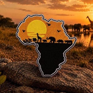 May include: An Africa-shaped patch with a black base and a yellow and orange sunset scene. Silhouetted animals, including giraffes and elephants, are visible. The patch is outlined in white and sits on a rock.