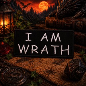 May include: A black patch embroidered with the words "I AM WRATH" in white. The patch is set against a fantasy backdrop with a dragon, books, and a full moon. A lantern and a compass rose are also visible.