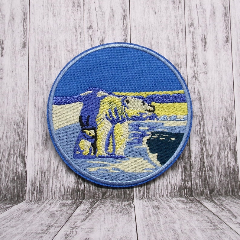 May include: Embroidered patch featuring a white polar bear and a smaller polar bear cub standing on a blue and white icy landscape with a yellow sunset in the background.