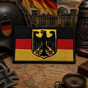 May include: A rectangular embroidered patch featuring the German flag with horizontal black, red, and gold stripes. Centered on the patch is a black eagle emblem with red claws and a red beak, rendered in a detailed, textured thread finish.
