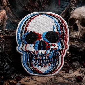 Puede incluir: Parche bordado de calavera con efecto 3D. La calavera presenta cuencas de ojos negras, contornos rojos y azules, y un fondo blanco. Ideal para ropa o accesorios.