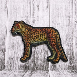 May include: A cheetah patch with a black outline and a detailed, realistic design. The cheetah is depicted in a standing position with a yellow, orange, and brown color scheme.