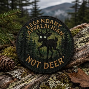 May include: A circular embroidered patch featuring a black silhouette of a deer-like creature with wide, white eyes. The text reads LEGENDARY APPALACHIAN and NOT DEER in gold lettering against a dark green forest background with pine trees.