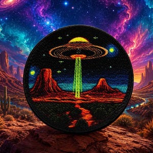 Può includere: Una toppa rotonda ricamata nera con un UFO sopra un paesaggio desertico. L'UFO emette un raggio di luce verde. Lo sfondo mostra una galassia colorata e montagne desertiche. La toppa è probabilmente per abbigliamento o accessori.