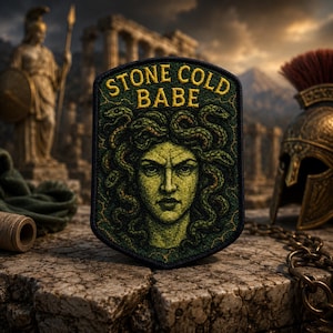 Puede incluir: Parche rectangular verde y amarillo con la inscripción «STONE COLD BABE» y una imagen de Medusa. El fondo muestra ruinas antiguas y un casco de bronce.