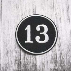 May include: A black and white embroidered patch with the number 13 in a white circle on a black background.