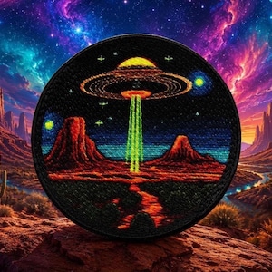 Pode incluir: Um emblema bordado circular apresentando um céu noturno escuro com um OVNI amarelo e laranja pairando sobre uma paisagem desértica vermelha. Um feixe de luz verde brilhante estende-se da nave até ao solo, rodeado por estrelas e planetas.