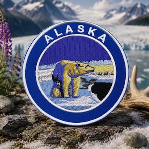 Może przedstawiać: Haftowana naszywka z niedźwiedziem polarnym i napisem "ALASKA" w białych literach na niebieskim tle. Naszywka ma niebieską obwódkę i przedstawia niedźwiedzia polarnego na lodzie z górskim tłem.