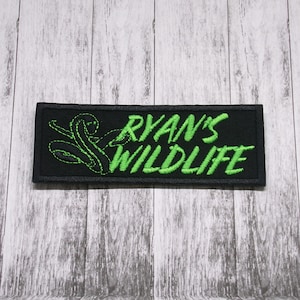 Può includere: Toppa ricamata nera con testo verde che recita "Ryan's Wildlife". Un serpente verde è ricamato sul lato sinistro della toppa.
